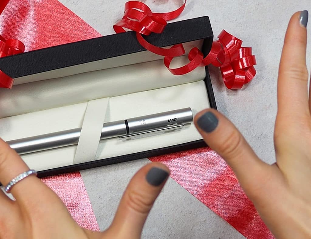 Silver Lamy Pur fountain pen with 'TS' engraved on the lid, in a gift box with decorations and 'surprised' hand gesture.